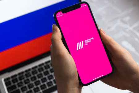 Poltava, Ukraine - April 8, 2022: Woman uses TV Rain app, Russia flag background. Blocked news application in Russian Federation, mobile phone with icon close-up view photoのeditorial素材