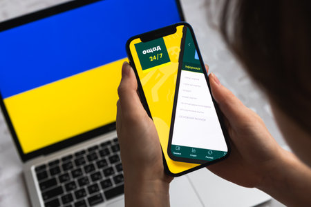 Poltava, Ukraine - April 8, 2022: Oschad bank in Ukraine. Mobile banking app for Ukraine users. Flag background, mobile phone with icon close-up view photのeditorial素材