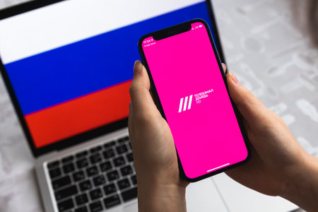 Poltava, Ukraine - April 8, 2022: Woman uses TV Rain app, Russia flag background. Blocked news application in Russian Federation, mobile phone with icon close-up view photoのeditorial素材