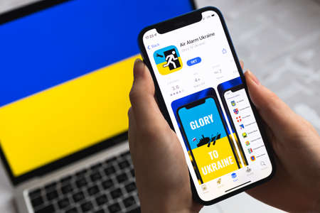 Poltava, Ukraine - April 8, 2022: Person Air Raid Siren app for mobile phone. Smartphone with modern air alarm application for Ukraine. Flag on backgroundのeditorial素材