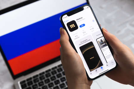 Poltava, Ukraine - April 8, 2022: Woman uses Meduza app, Russia flag background. Blocked news application in Russian Federation, mobile phone with icon close-up view photoのeditorial素材