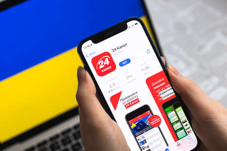 Poltava, Ukraine - April 8, 2022: 24 Channel Ukraine News app for mobile phone. Woman uses mobile application close-up view with flag backgroundのeditorial素材