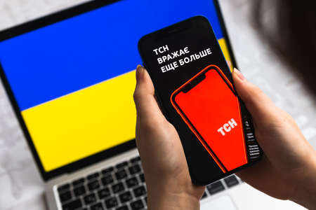 Poltava, Ukraine - April 8, 2022: Woman use TSN news app in Ukraine. Mobile phone in hands, flag backgroundのeditorial素材