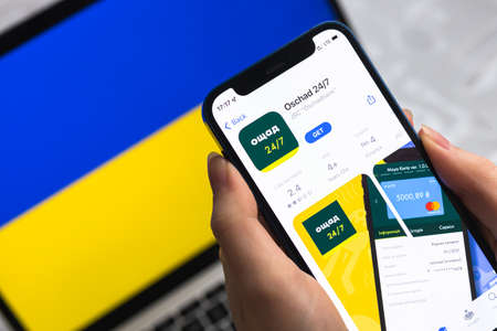 Poltava, Ukraine - April 8, 2022: Oschad bank in Ukraine. Mobile banking app for Ukraine users. Flag background, mobile phone with icon close-up view photのeditorial素材