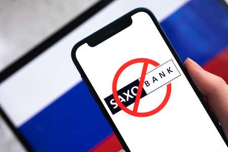 SPB, Russia - April 9, 2022: Saxo Bank in Russia. Blocked and banned company on Russian flag background. mobile phone in hand close-up viewのeditorial素材