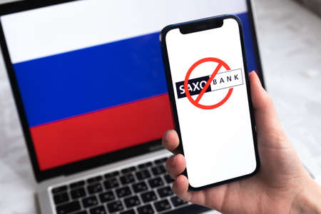 SPB, Russia - April 9, 2022: Saxo Bank in Russia. Blocked and banned company on Russian flag background. mobile phone in hand close-up viewのeditorial素材
