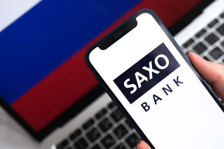 SPB, Russia - April 9, 2022: Saxo Bank in Russia. Russian flag background. mobile phone in hand close-up viewのeditorial素材