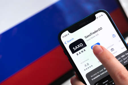 SPB, Russia - April 9, 2022: Saxo app icon close-up. Blocked and banned company on Russian flag background. mobile phone in hand close-up viewのeditorial素材