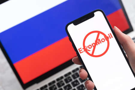 SPB, Russia - April 8, 2022: Exxonmobil in Russia. Blocked and banned service, EU sanctions. Mobile phone with , russian flag background photoのeditorial素材
