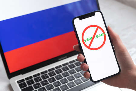 SPB, Russia - April 8, 2022: Sberbank and sanctions. Blocked Russian bank,  and ban symbol on mobile phone screen and flag backgroundのeditorial素材