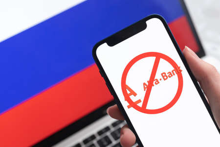 SPB, Russia - April 8, 2022: Alfabank and sanctions. Blocked Russian bank, and ban symbol on mobile phone screen and flag backgroundのeditorial素材