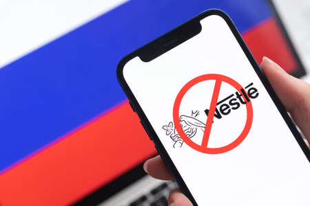 SPB, Russia - April 8, 2022: Nestle in Russia. Blocked and banned service, EU sanctions. Mobile phone with , russian flag background photoのeditorial素材