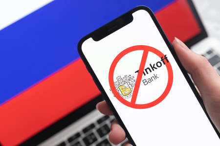 SPB, Russia - April 8, 2022: Tinkoff Bank and sanctions. Blocked Russian bank, and ban symbol on mobile phone screen and flag backgroundのeditorial素材