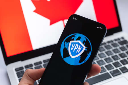 VPN in Canada. Secure and safe internet concept. privacy. Hand with mobile phone and VPN application. Flag and laptop on the background photoの写真素材