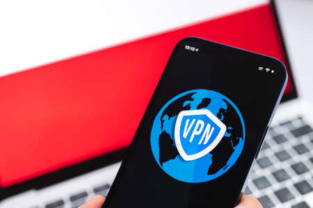 VPN in Poland. Secure and safe internet concept. privacy. Hand with mobile phone and VPN application. Flag and laptop on the background photoの写真素材