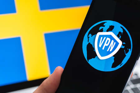 VPN in Sweden. Secure and safe internet concept. privacy. Hand with mobile phone and VPN application. Flag and laptop on the background photoの写真素材