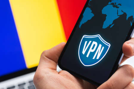 VPN in Romania. Secure and safe internet concept. privacy. Hand with mobile phone and VPN application. Flag and laptop on the background photoの写真素材