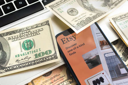 Poltava, Ukraine - April 28, 2022: Etsy shopping app on mobile phone screen. Business background with laptop and moneyのeditorial素材