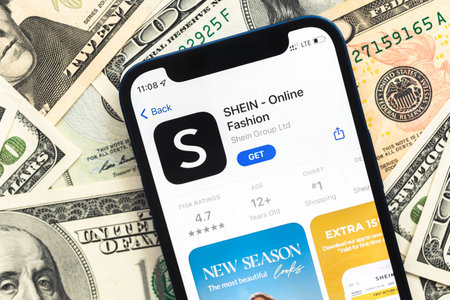 Poltava, Ukraine - April 28, 2022: Shein fashion shopping app on mobile phone screen. Business background with dollar money banknotesのeditorial素材