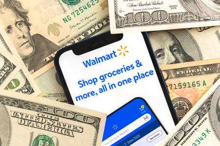 Poltava, Ukraine - April 28, 2022: Walmart app on mobile phone screen. Business background with laptop and moneyのeditorial素材