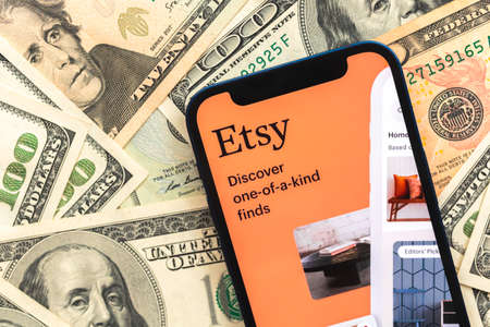 Poltava, Ukraine - April 28, 2022: Etsy shopping app on mobile phone screen. Business background with dollar money banknotesのeditorial素材