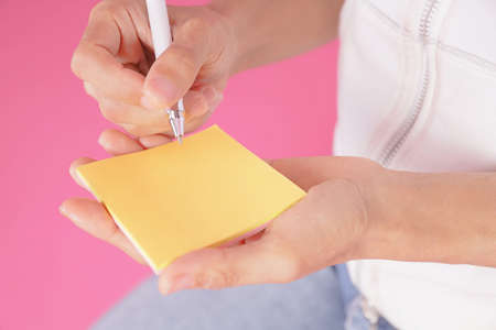 woman writing message on yellow note paper.with white pen on the empty space in the note paperの写真素材