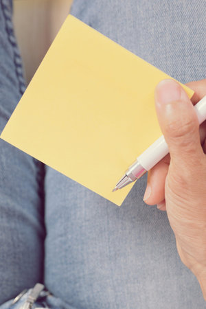 woman writing message on yellow note paper.with white pen on the empty space in the note paper