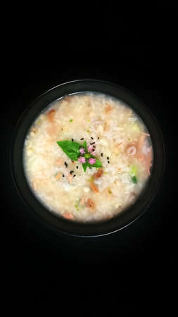 Rice soup with spices and chicken on a bowl and black background.set up light in studio.Decorated with pink flowers and basil.の写真素材
