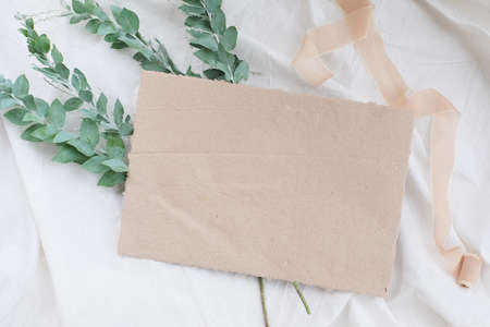 Photostock wedding styled composition. Feminine desktop mockup scene with leaves, silk ribbon, blank greeting card on white textured fabric background. Flat lay, top view.の写真素材