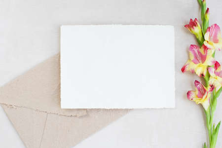 Photostock composition. Feminine desktop mockup scene with leaves, Amaryllis flower, silk ribbon, brown envelope, blank greeting card on white textured concrete background. Flat lay, top viewの写真素材