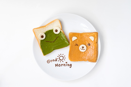 Top view of cute breakfast for kids, green tea spread and peanut butter design to frog and bear on breads with good morning text on white backgroundの写真素材