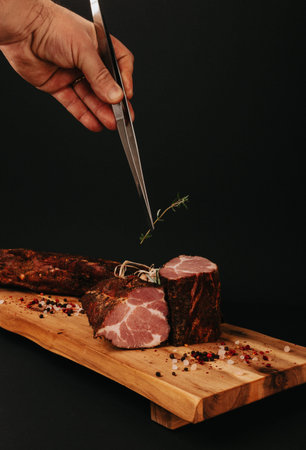 Smoked pork muscles sausage and bacon on a wooden board with the addition of fresh aromatic herbs,...