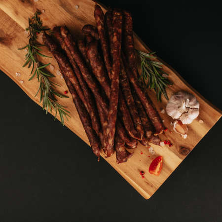 Smoked pork muscles sausage and bacon on a wooden board with the addition of fresh aromatic herbs, garlic, sea salt and pepper.の写真素材