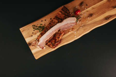 Smoked pork muscles sausage and bacon on a wooden board with the addition of fresh aromatic herbs, garlic, sea salt and pepper.の写真素材