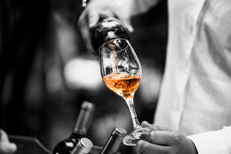 The waiter serves rose, red and white wine from the wine bottle in the wine glass at an event.の写真素材