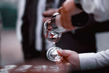 The waiter serves rose, red and white wine from the wine bottle in the wine glass at an event.の写真素材