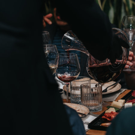 Elegant waiter pours red wine from bottle into glass at restaurant. Sommelier tasting wine in restaurant. Copy space for text menu elegant or recipe on dark background.の写真素材