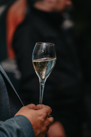 Elegant waiter pours champagne from bottle into glass at restaurant. Sommelier tasting white...