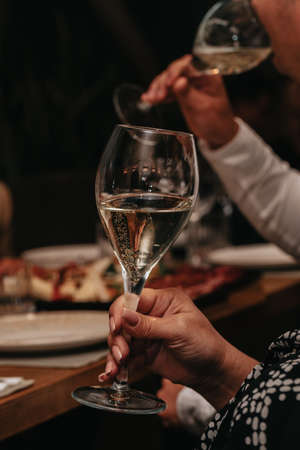 Elegant waiter pours champagne from bottle into glass at restaurant. Sommelier tasting white sparkling wine in restaurant. Copy space for text menu elegant or recipe on dark background.の写真素材