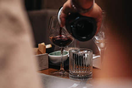 Elegant waiter pours red wine from bottle into glass at restaurant. Sommelier tasting wine in restaurant. Copy space for text menu elegant or recipe on dark background.の写真素材