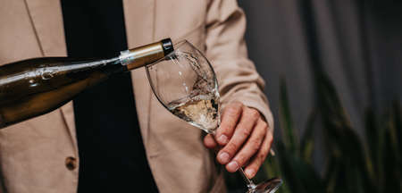 Elegant waiter pours champagne from bottle into glass at restaurant. Sommelier tasting white sparkling wine in restaurant. Copy space for text menu elegant or recipe on dark background.の写真素材