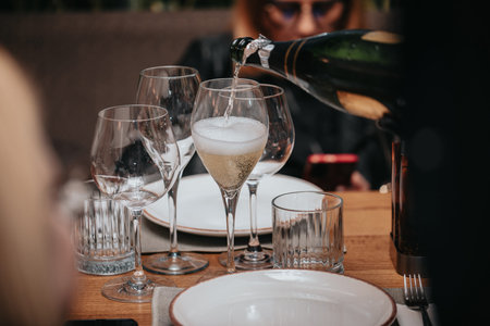 Elegant waiter pours champagne from bottle into glass at restaurant. Sommelier tasting white...