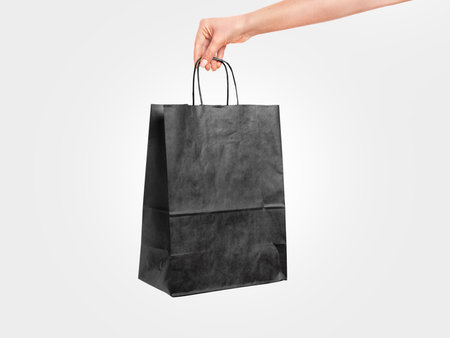 Black paper bag in female hand isolated on white background.の写真素材
