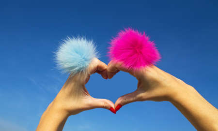 Fingers heart with blue and pink rings with fur on blue sky background.の写真素材