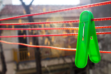 green clothespin hangs on the red clothesline on the backyard in the morningの写真素材