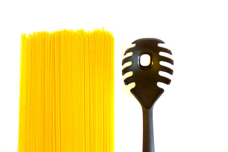 Long raw yellow spaghetti and black spoon with hole isolated on white backgroundの写真素材