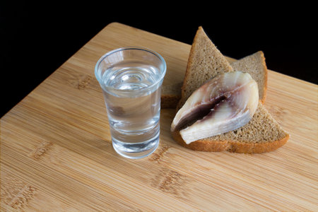Glass with vodka and appetizer with sprat and bread. Black background. Shot.
