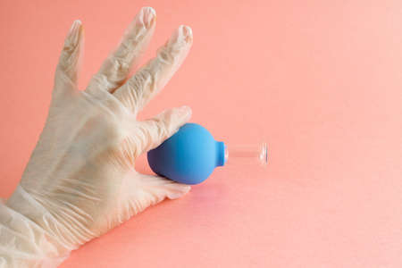 female hand with French manicure in medicine glove holds blue cosmetic medical jar for vacuum facial massage on pink background, latex or rubber and glass.の写真素材