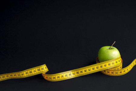 Green apple and measuring tape  with centimeters and inches isolated on black background.