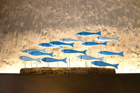 A group of wooden blue and turkuoise fish on metal spokes on a wooden podium with white textures wallの写真素材